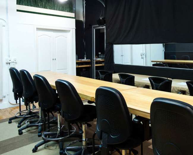 The image shows a large conference room with a long wooden table and several black swivel chairs arranged around it, facing a mirror on the wall.