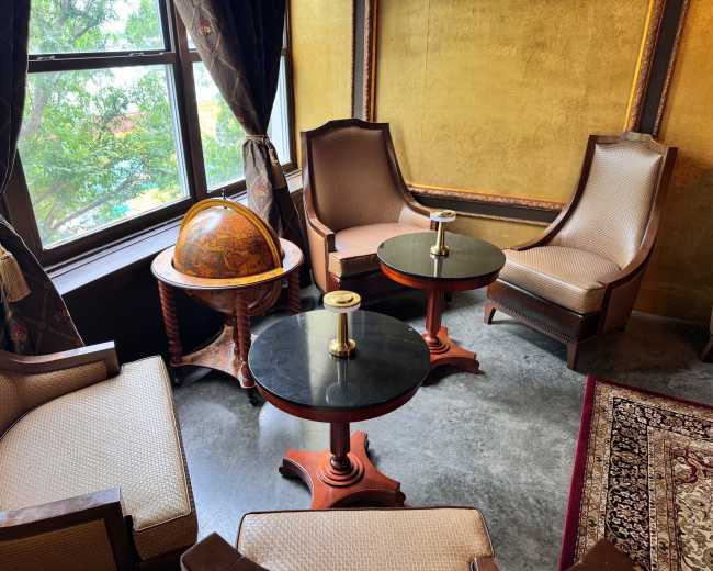 The image shows a cozy seating area with two armchairs and two small circular tables near a window, accompanied by a decorative globe on a stand.