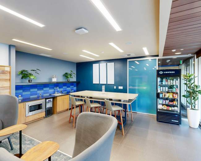 The image shows a modern kitchenette area featuring a blue tiled backsplash, a countertop with seating, and a refrigerator with a glass front.