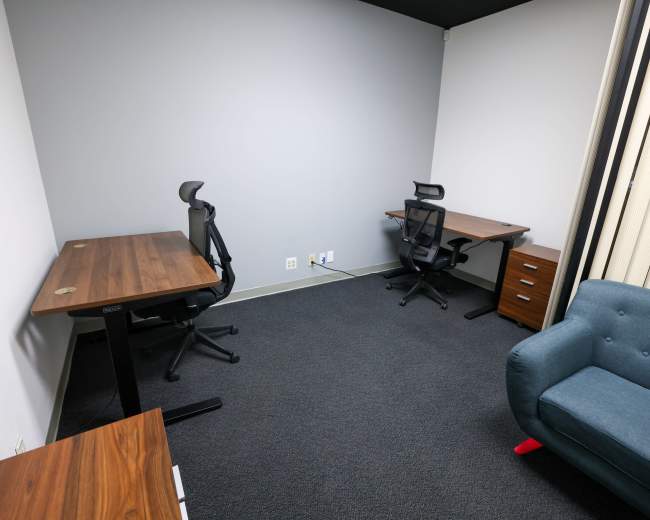 A small office space with two desks, ergonomic chairs, and a blue couch against the wall.