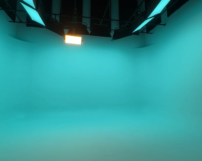 The image shows an empty studio space with a bright teal backdrop and overhead lighting.