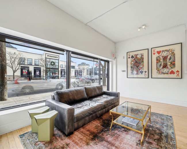 A modern living space features a dark leather sofa and a glass coffee table, with large windows showing a street view outside.
