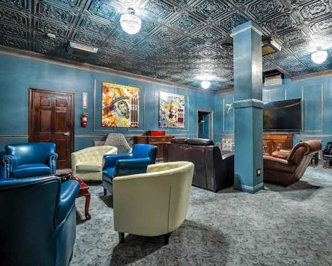 The image shows a cozy lounge area with various seating options, including leather and upholstered chairs, surrounded by blue walls and colorful artwork.