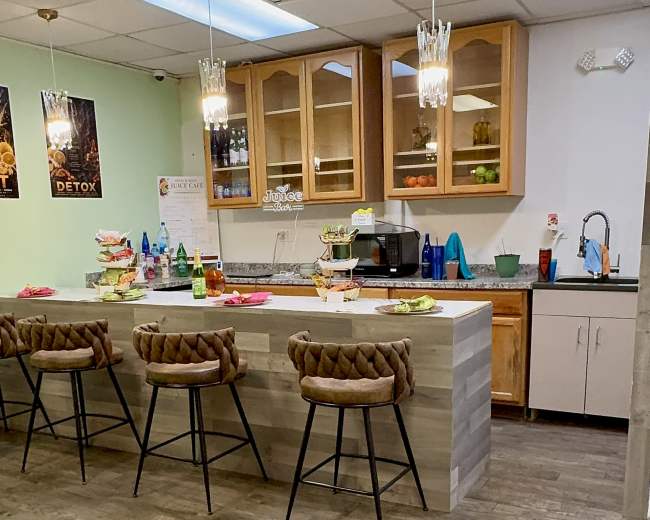 The image shows a modern kitchen area with a bar counter and several bar stools, where various food items and beverages are arranged on the counter.