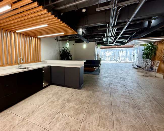 The image shows a modern kitchen area with a long countertop, cabinets, and wooden slat walls, leading to a spacious corridor.
