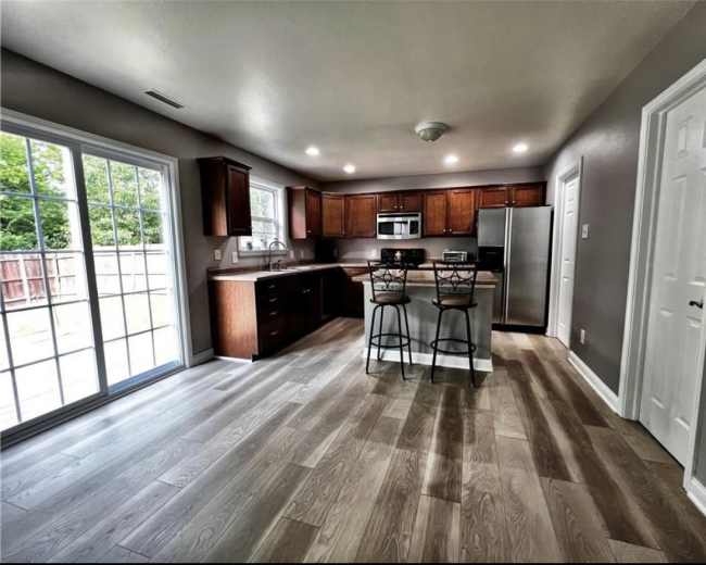 The image shows a modern kitchen with wooden cabinetry, stainless steel appliances, and a sliding glass door leading to an outdoor space.