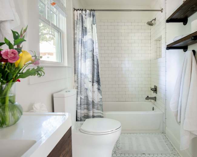 The image shows a neatly arranged bathroom featuring a white tiled shower, a bathtub, a toilet, and a vase of flowers on the sink.