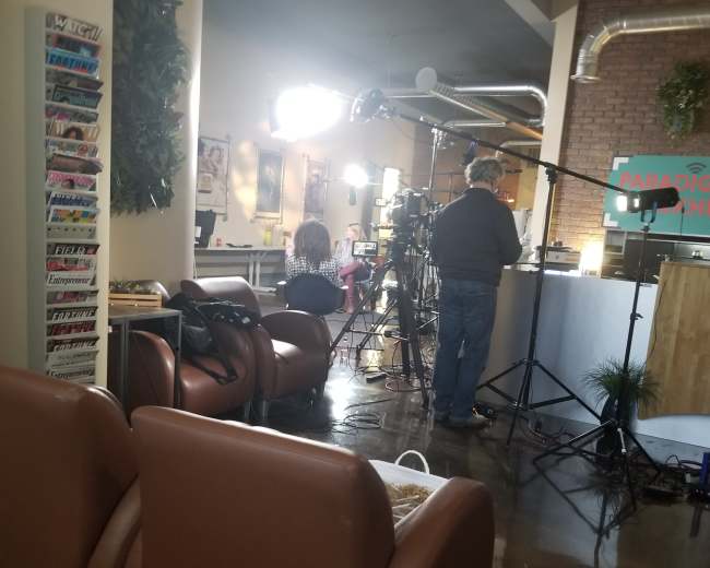 A filming setup in a cafe, with crew members and equipment arranged around a seating area.