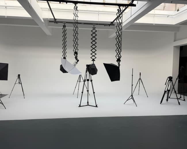The image shows a photography studio featuring various lighting equipment and tripods set up on a seamless white backdrop.