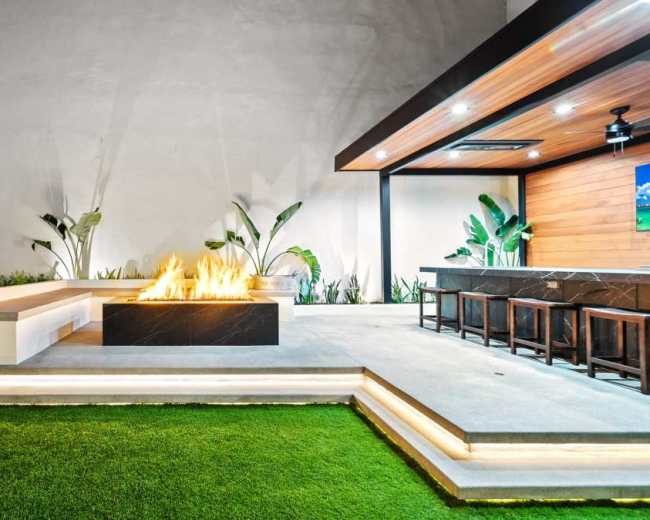 The image features a modern outdoor patio with a fire pit, seating area, and lush greenery.