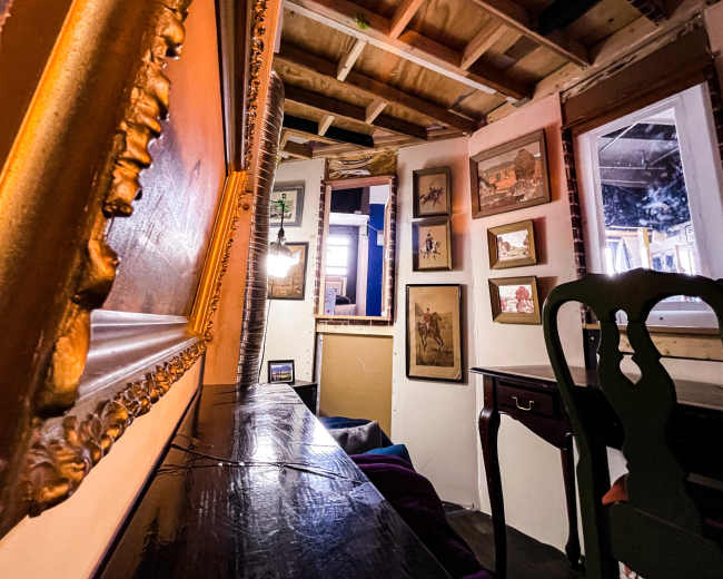 A cozy interior of a room with wooden beams, framed artwork on the walls, and a dark table with a green chair.