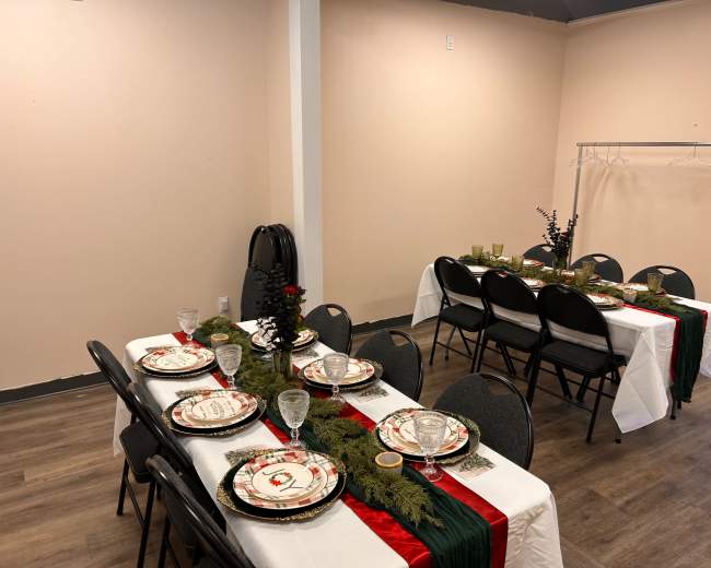 A dining area is set up with two long tables, each adorned with decorative tableware, green garlands, and red accents.
