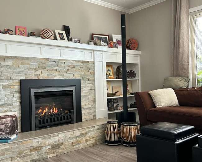 A modern living room with a stone fireplace, a dark sofa, a tall black speaker, and decorative items on the shelves and mantel.