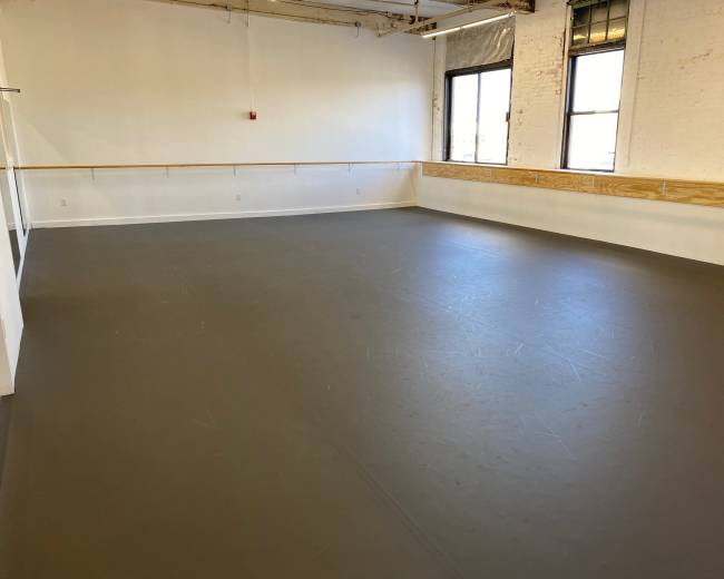 An empty dance studio with a smooth gray floor and large windows.