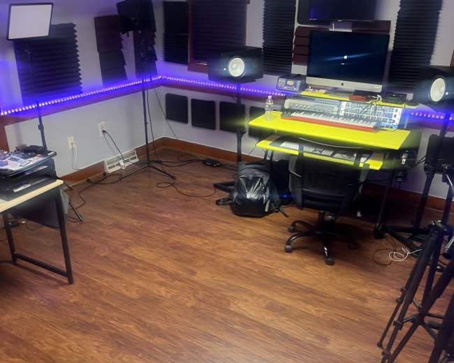 The image shows a music studio with a mixing console, speakers, and LED lighting along the walls.