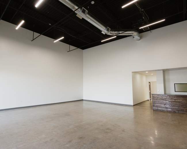 The image shows an empty interior space with a high ceiling, concrete flooring, and a doorway leading to another room.