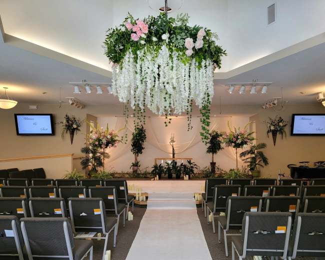 A decorated indoor ceremony space featuring floral arrangements, a central altar with a candle, and seating arranged in rows facing the front.