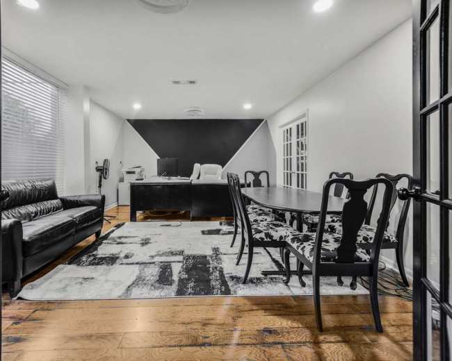 The image shows a modern office with a black and white color scheme, featuring a large desk, a couch, and a dining table surrounded by chairs.