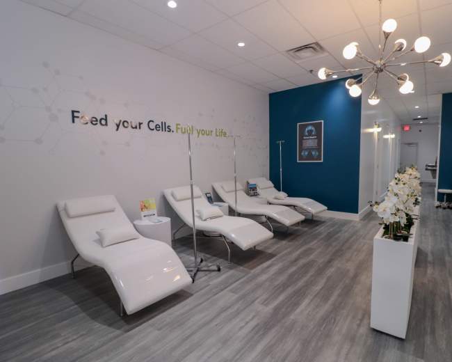 The image shows a modern, well-lit wellness center with white reclining chairs and a decorative plant arrangement, along with motivational wall art.