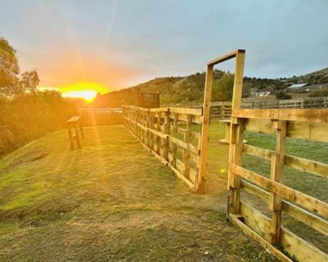 The image shows a wooden corral with a sunset in the background, casting warm light over the landscape.