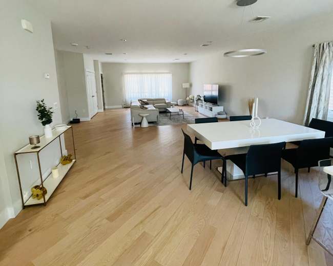 A modern living and dining area with light wood flooring, a large dining table surrounded by black chairs, and a cozy seating arrangement in front of a television.