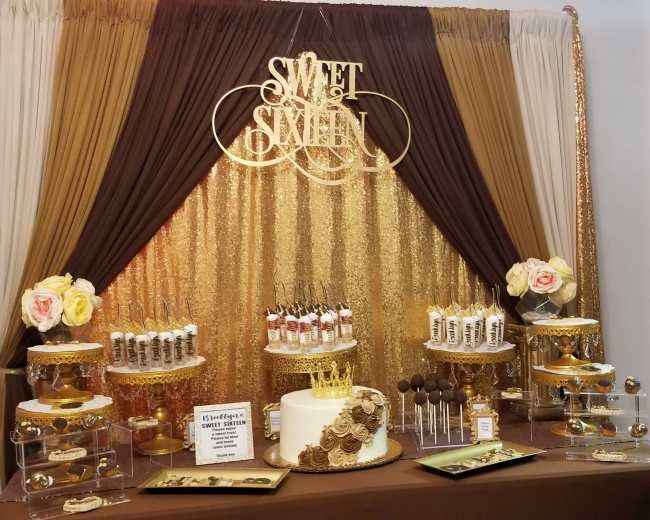A dessert table decorated with gold and brown drapery, featuring an assortment of cakes, pastries, and decorative elements for a "Sweet Sixteen" celebration.