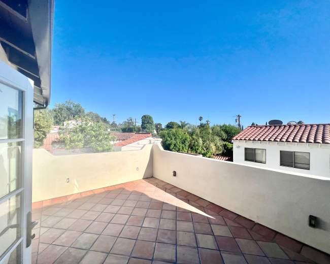 The image shows a tiled rooftop terrace with a clear blue sky and adjacent rooftops in the background.