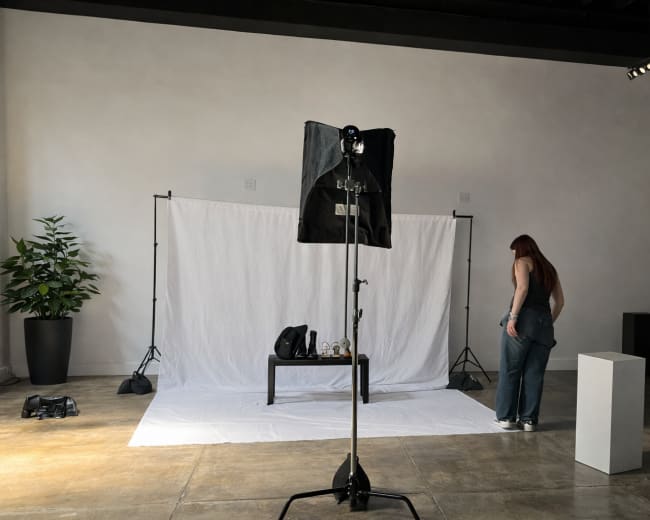 A woman stands beside a white backdrop in a spacious, well-lit photography studio.