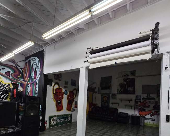 The image shows an indoor space featuring graffiti art on the walls, a tiled floor, and a few furniture pieces, including speakers and couches.