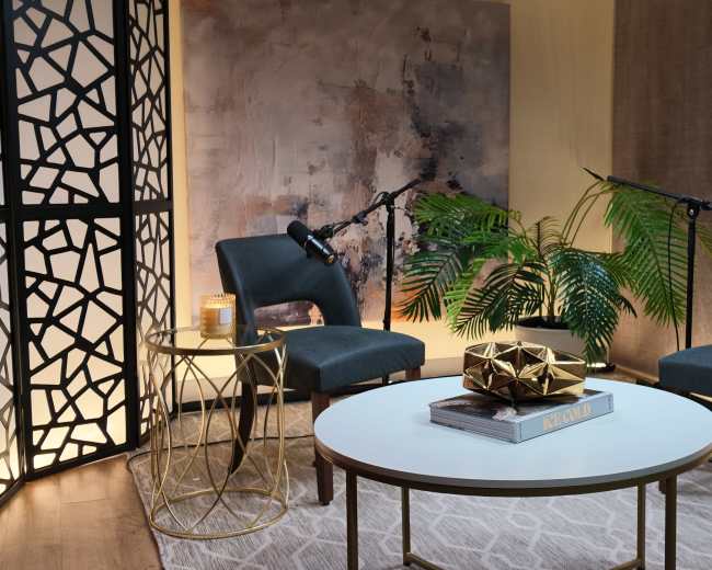 The image depicts a cozy interview setup with two chairs facing each other, a small round table adorned with decorative items, and soft lighting accentuated by plants in the background.