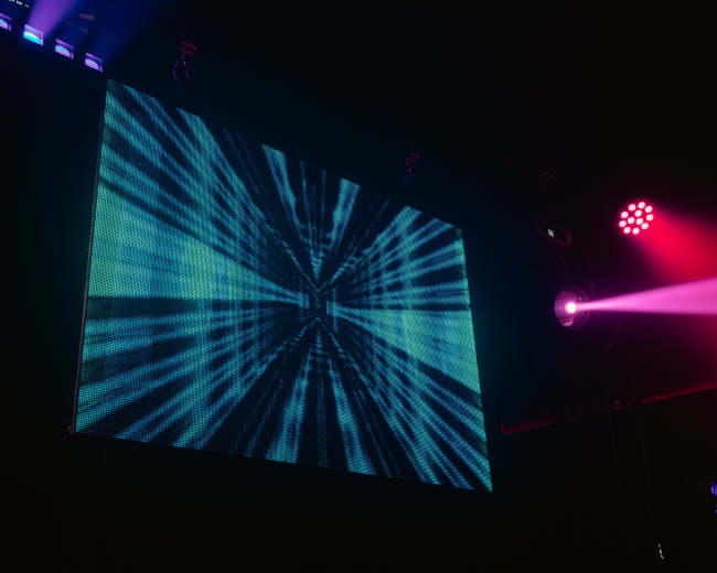 A large screen displays a digital pattern of blue and green lines radiating from a central point.