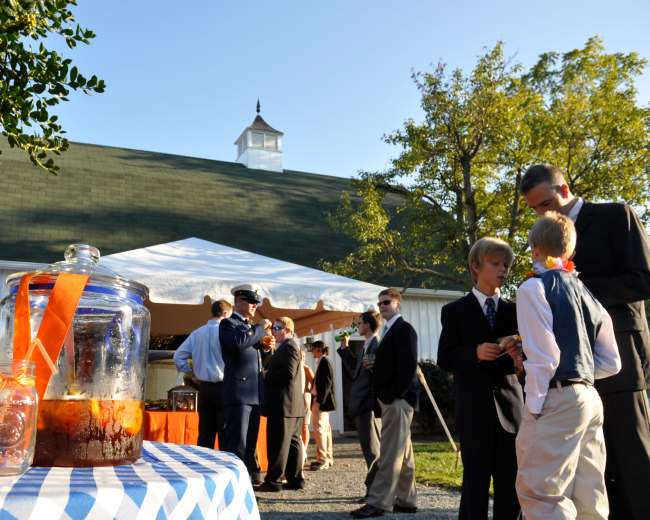 A group of men dressed in formal attire socialize near a beverage station outside a large tented area.