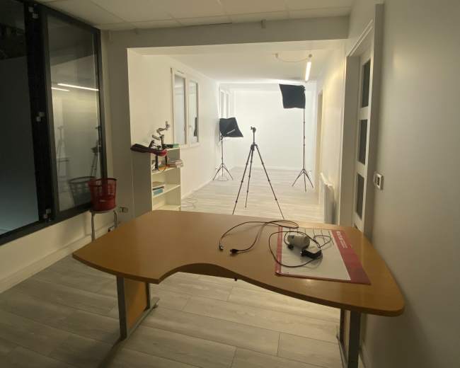 The image shows a brightly lit room with a wooden table in the foreground and two light stands positioned in the background.