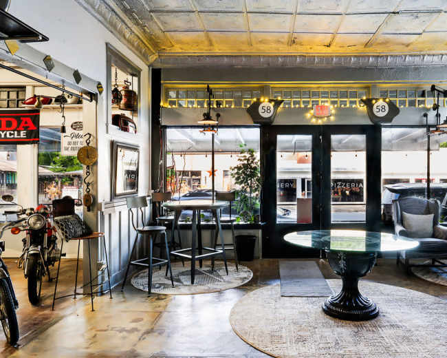 The image shows a stylish cafe interior with a circular glass table, seating arrangements, and large windows that let in natural light.