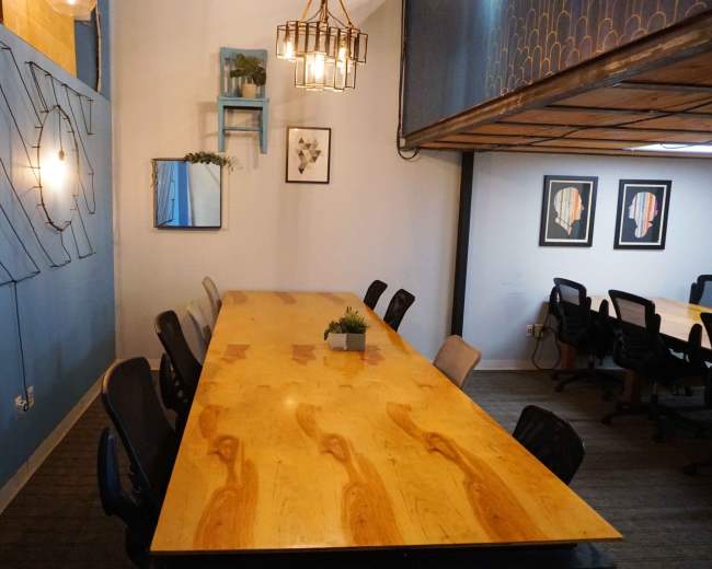 The image shows a conference room with a long wooden table, black office chairs, and blue walls featuring decorative elements.