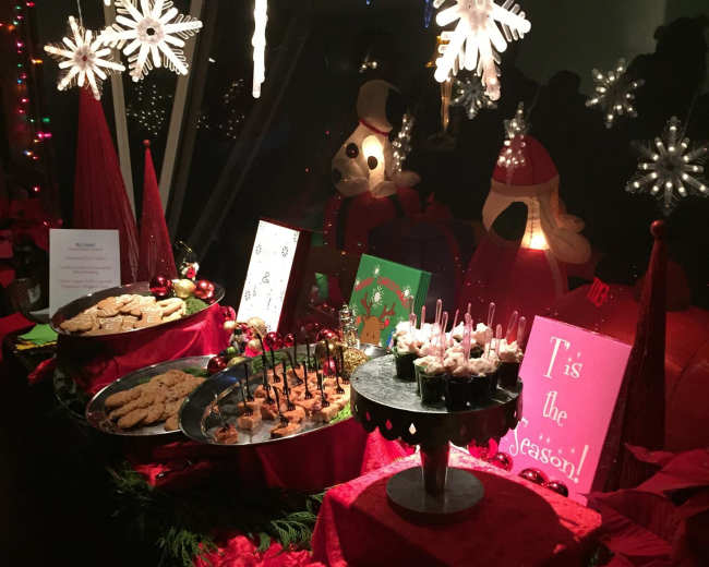 A festive table displays an array of holiday treats surrounded by decorations, including snowflakes and red foliage.