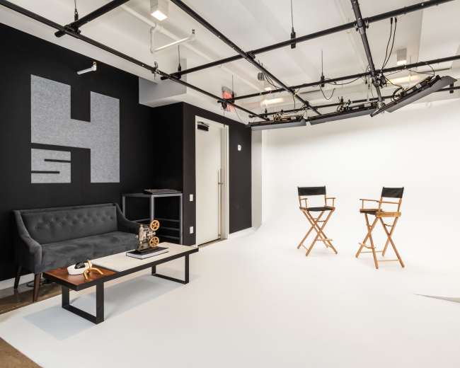 A minimalist studio space featuring two director's chairs in front of a white backdrop, accompanied by a black couch and a coffee table.