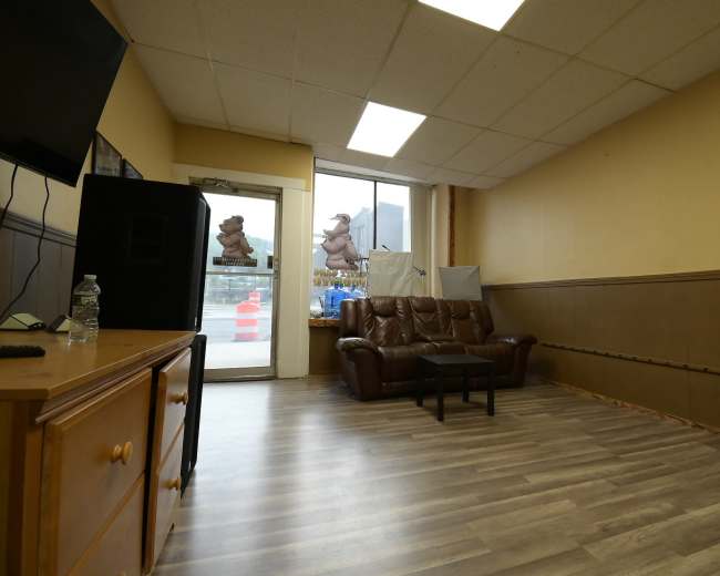 The image shows a sparsely furnished room with a brown leather couch, a small black table, and a door leading outside.