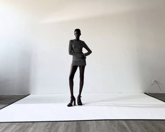 A tall model stands on a white backdrop in a spacious, brightly lit studio.