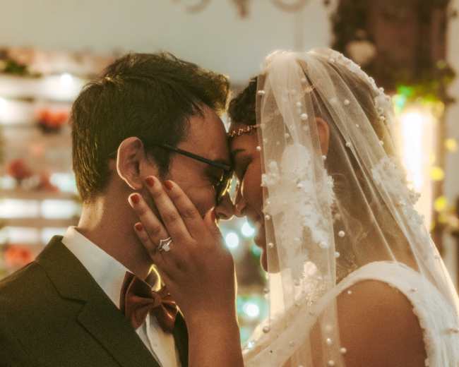A couple shares a close moment at their wedding, with their foreheads touching and hands gently clasped.