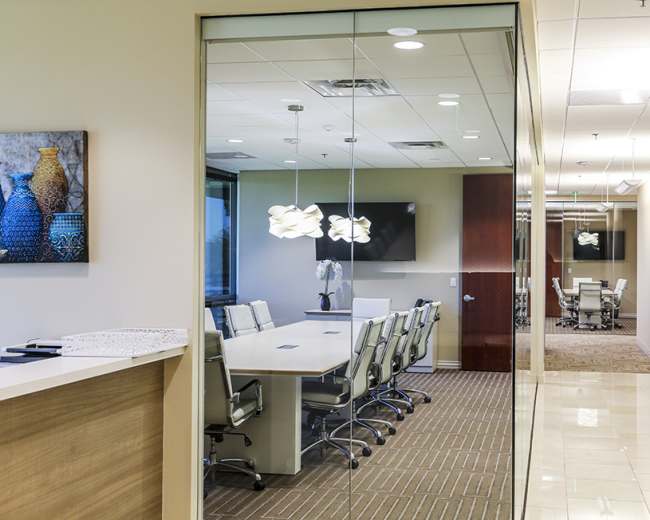 The image shows a modern office environment featuring a conference room with a long table and ergonomic chairs, visible through glass walls.