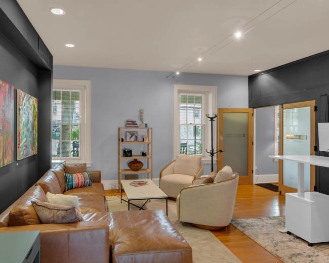 The image shows a modern living room with leather sofas, abstract artwork on the walls, and a stylish, minimalist decor.