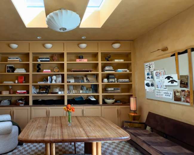 The image shows a well-organized room with a wooden table at its center, surrounded by shelves filled with various items and a mannequin in the corner.