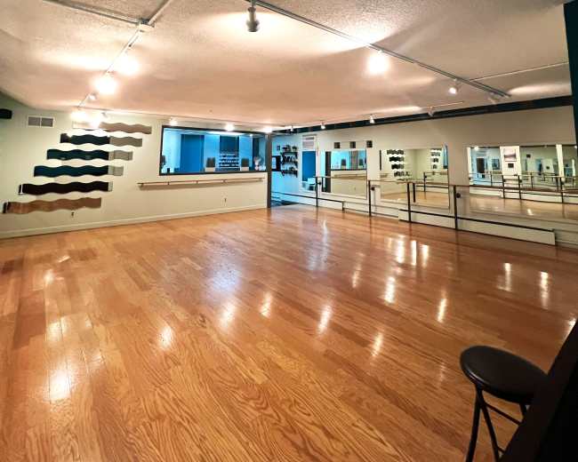 A spacious dance studio with wooden flooring, mirrors along the walls, and track lighting.