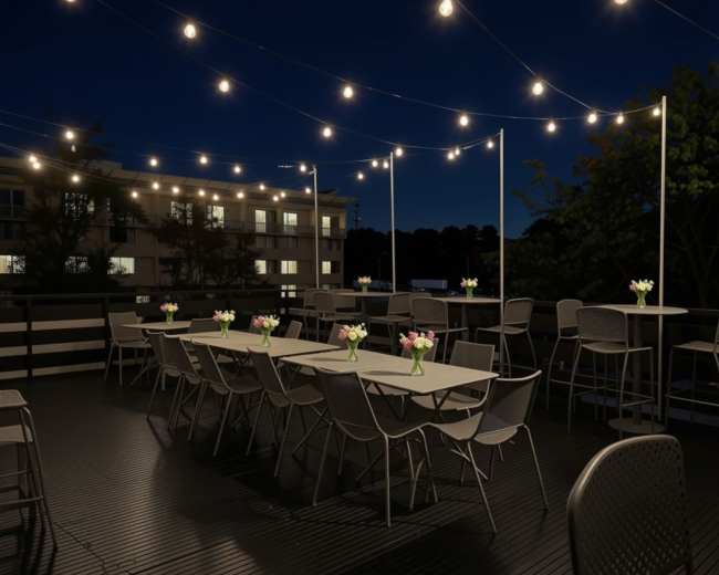 The image shows a rooftop dining area at night, featuring tables with flower centerpieces and string lights illuminating the space.