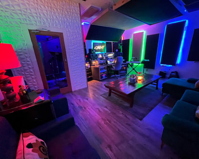 The image shows a music studio with colorful LED lighting, a mixing desk, and various musical equipment, surrounded by a seating area.