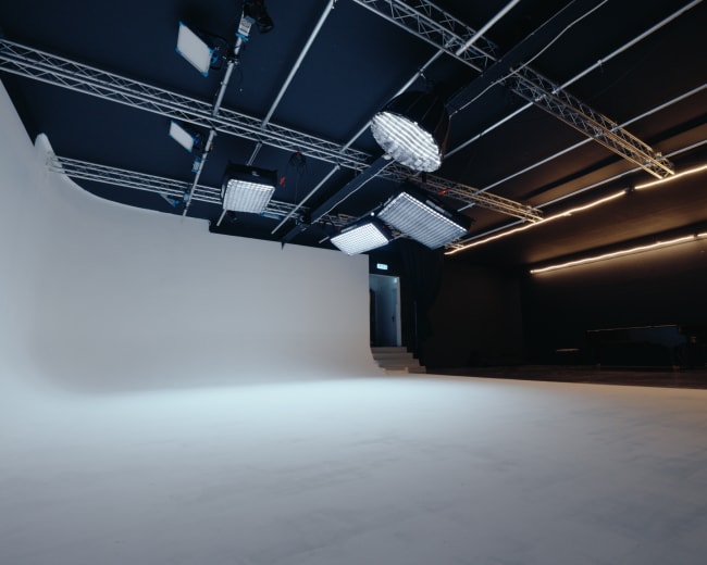 The image shows a large, empty studio space with a smooth white backdrop and multiple lighting setups overhead.