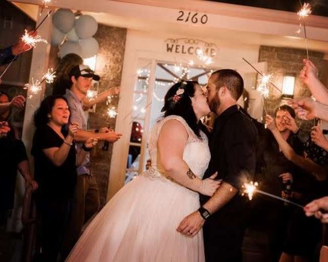 A bride and groom kiss while surrounded by guests holding sparklers in celebration.
