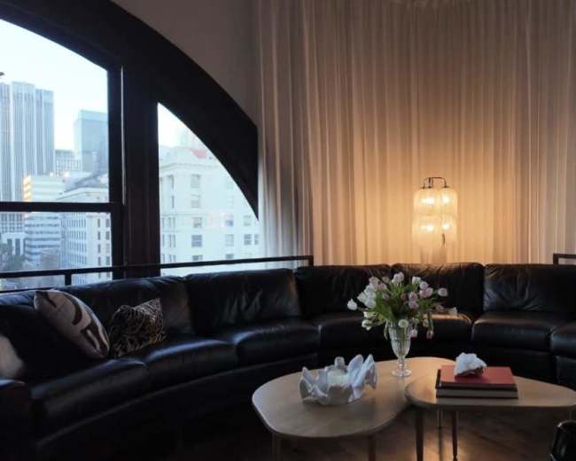 A curved leather sectional sofa surrounds a coffee table with a floral arrangement in a well-lit room featuring large arched windows.