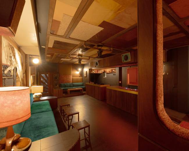 The image shows a dimly lit lounge area with a bar, plush seating, and decorative acoustic panels on the ceiling.